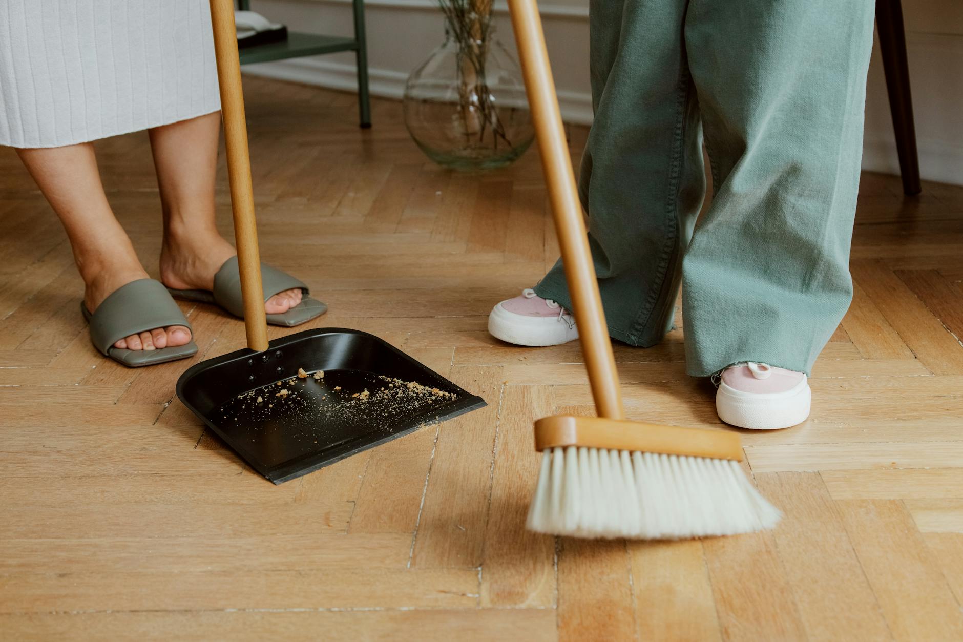 Osoby zamiatające drewnianą podłogę miotłą i szufelką w mieszkaniu