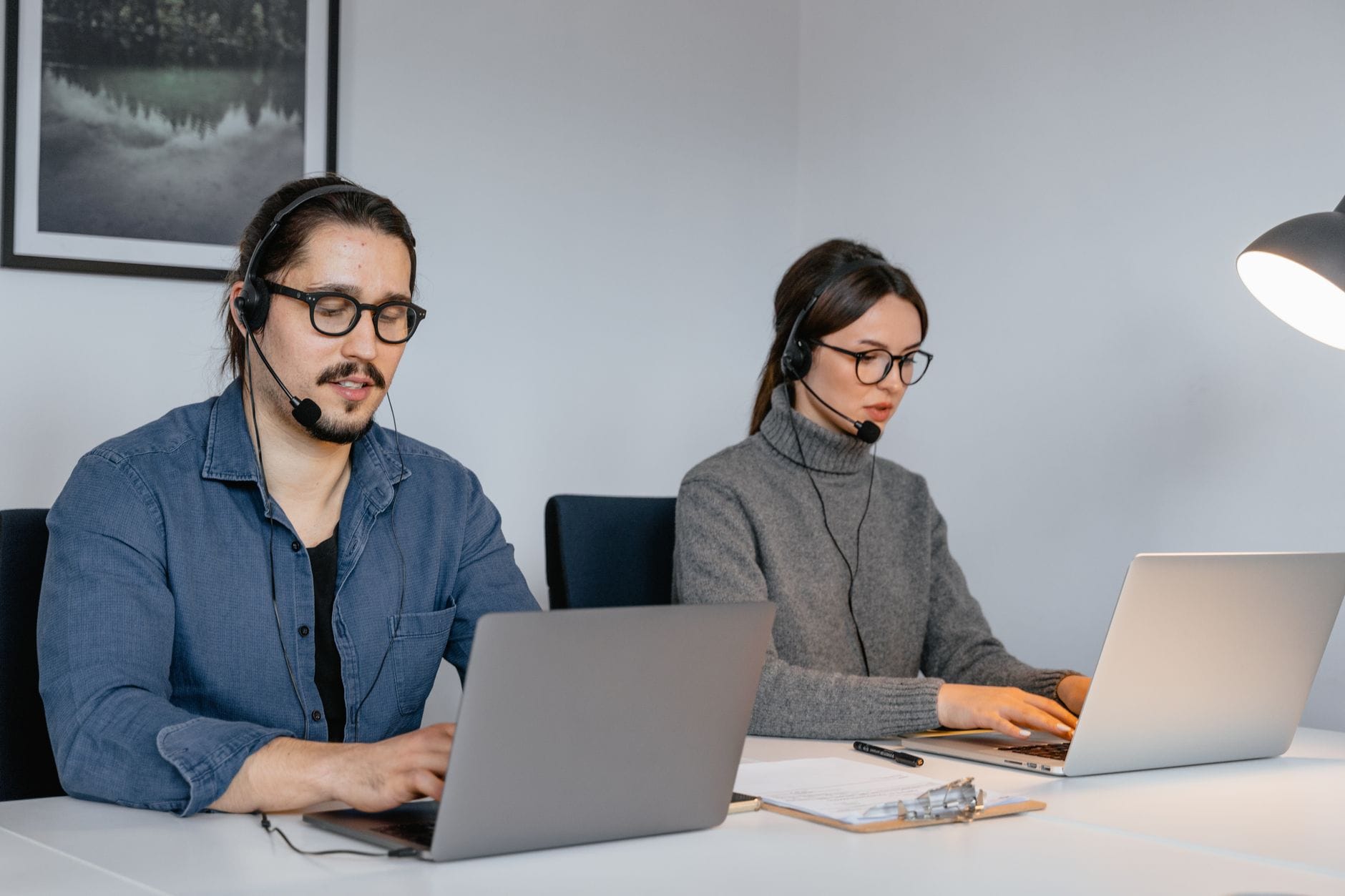 Dwoje pracowników IT w słuchawkach uczy się angielskiego online przy laptopach