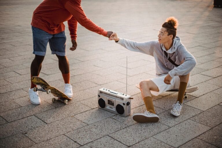 Dwóch mężczyzn przybija piątkę obok deskorolki i boomboxa
